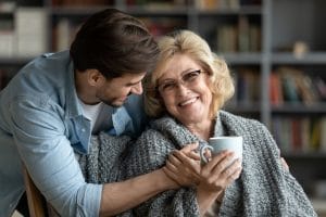 Happy middle-aged mother relax in chair drink tea enjoy family weekend reunion with grown-up son